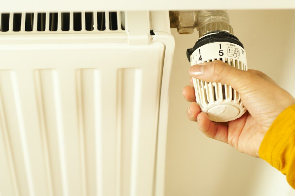 person adjusting a thermostatic radiator valve (TRV) device on a steam heating radiator